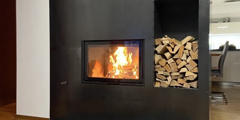 Ein warmes Feuer brennt in einem Ofen aus Stahl mit einem bequem aussehenden Teppich und einer bereitstehenden Champagnerflasche